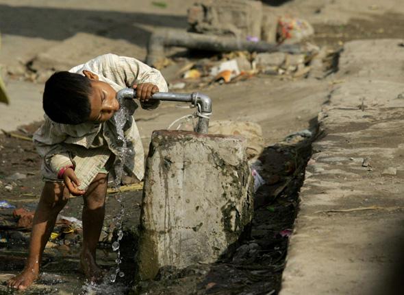 Un enfant boit de l'eau au robinet, en Inde, dans un quartier où l'eau potable n'arrive pas dans les maisons.
